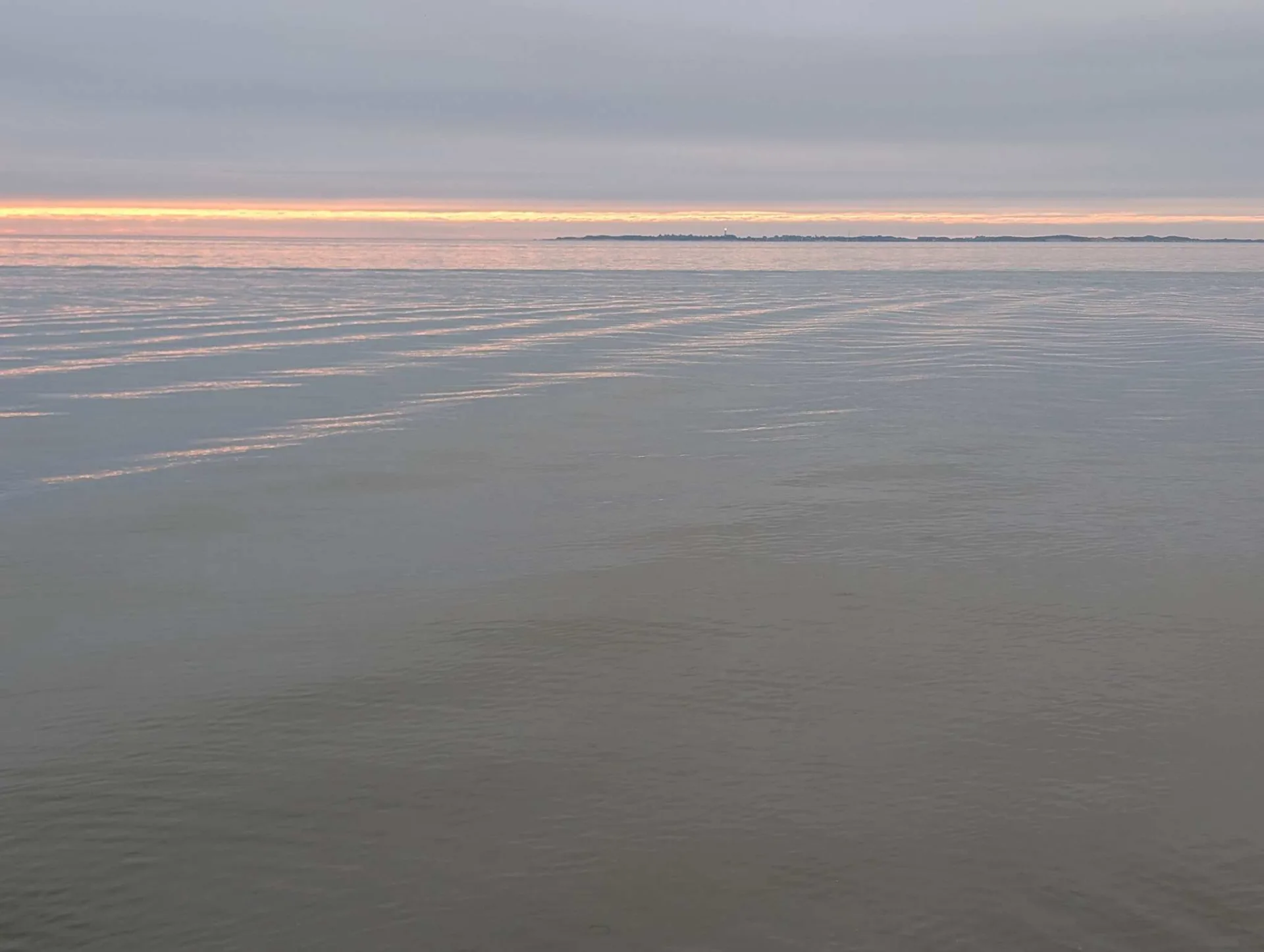 Abend überm Watt: ein schmaler Lichtstreif über Amrum, der Rest in stillem Grau.