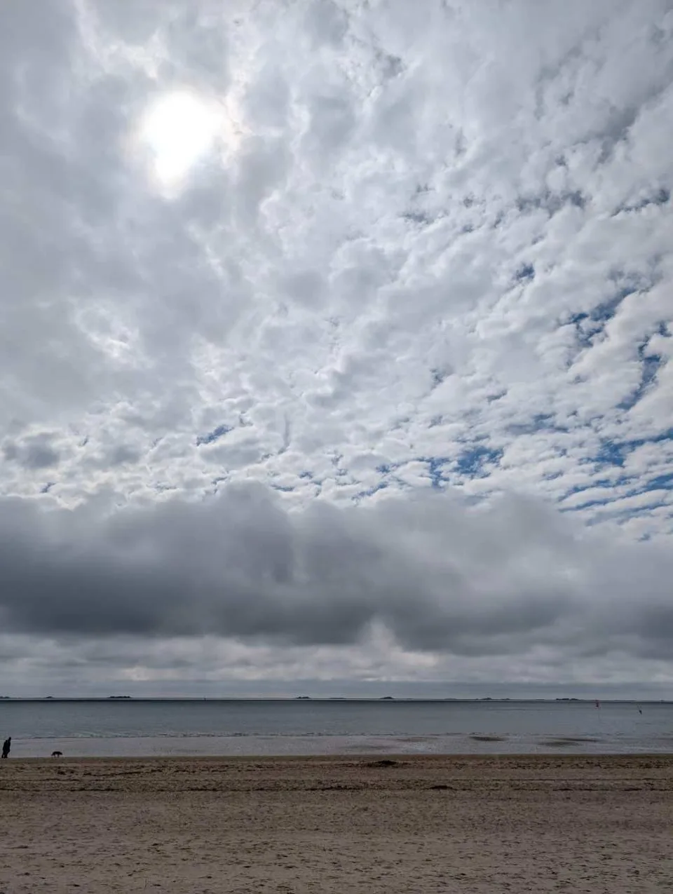 Weite und Himmel am Südstrand von Wyk – ein einzelner Spaziergänger mit Hund am Saum des ablaufenden Wassers.