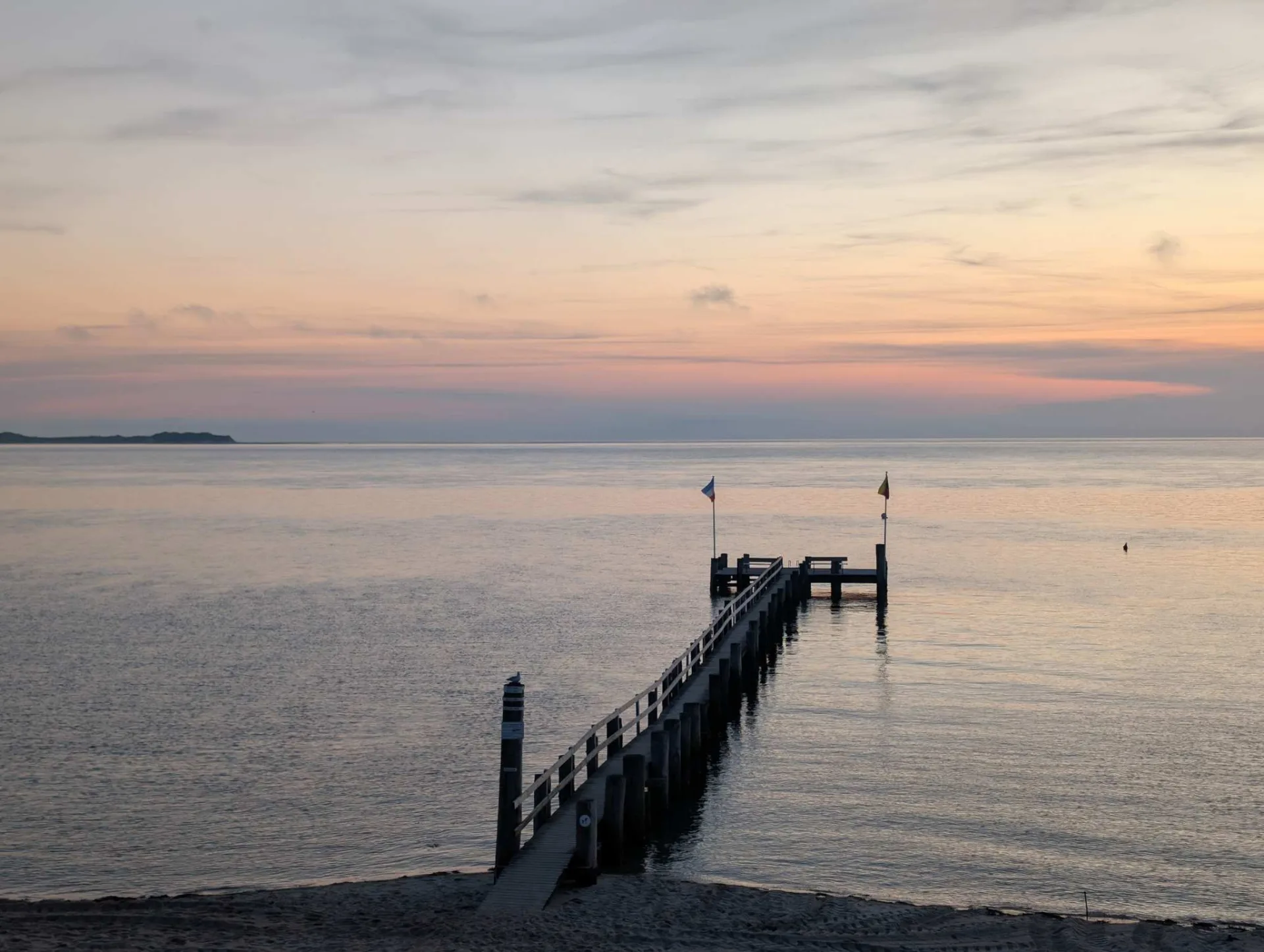 Der Badesteg von Utersum im Abendlicht, am Horizont die Silhouette von Amrum.