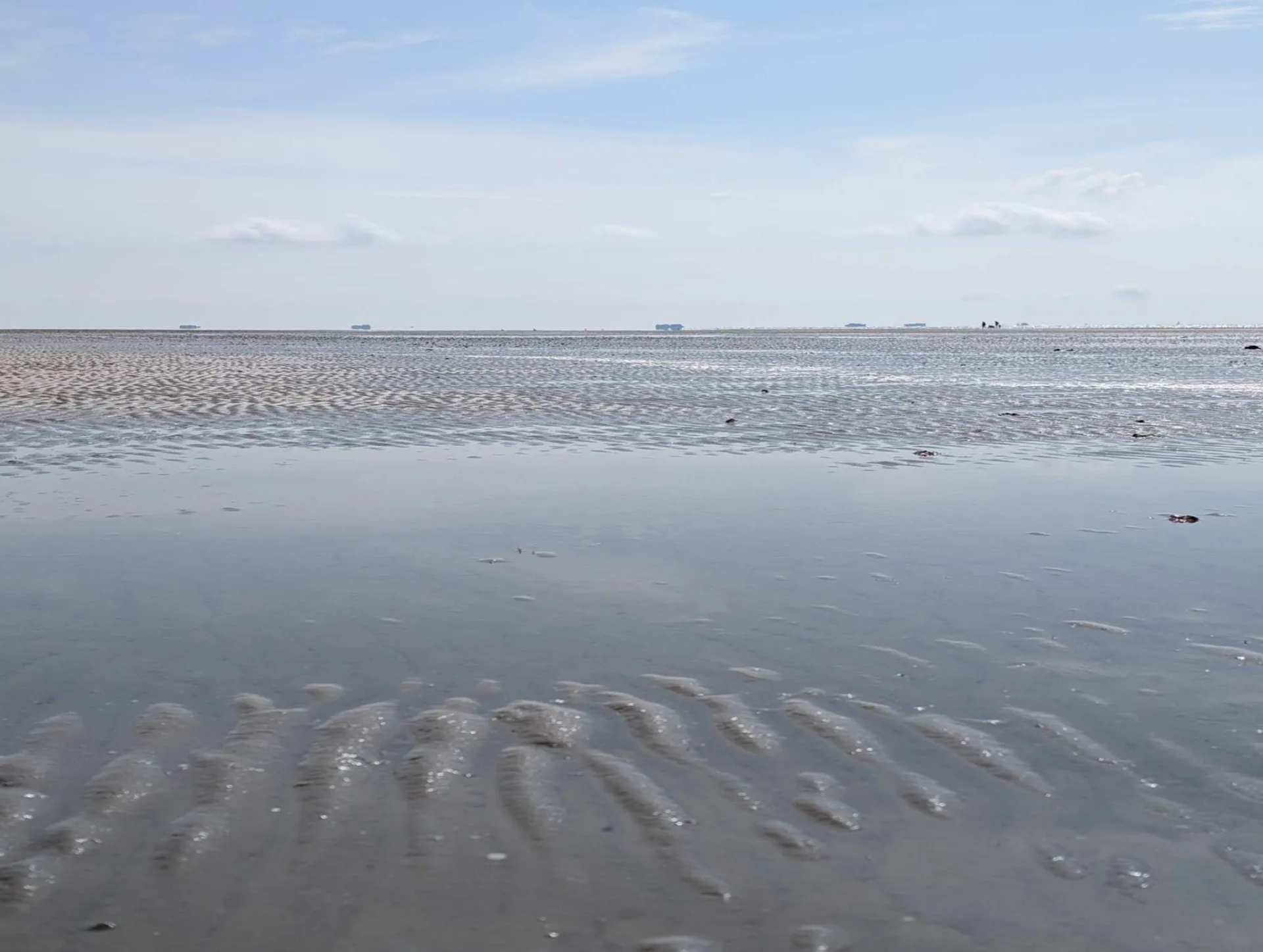Watt bei Niedrigwasser: geriffelter Sand und ein schmaler Priel unter weitem Aprilhimmel.