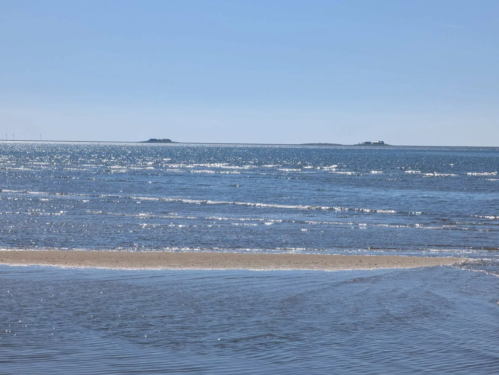 Sonnenfunkeln überm Watt am Südstrand, am Horizont flache Halligen und ferne Windräder.