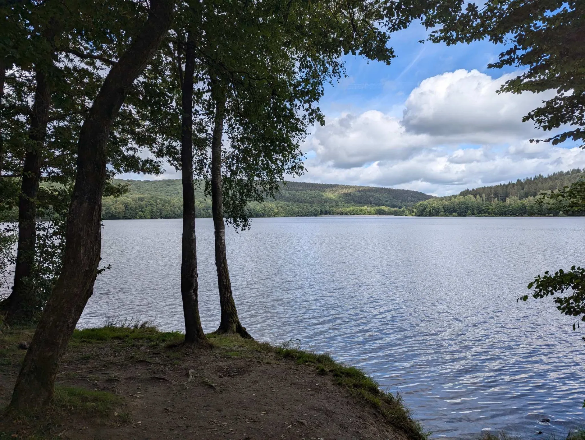 Sonniger Vormittag am See, Wolken ziehen über die bewaldeten Höhen.