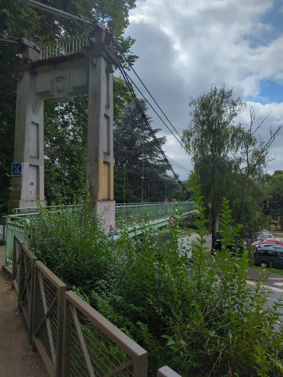 Eine alte Hängebrücke, das Wappen am Pylon, spannt über den Fluss.