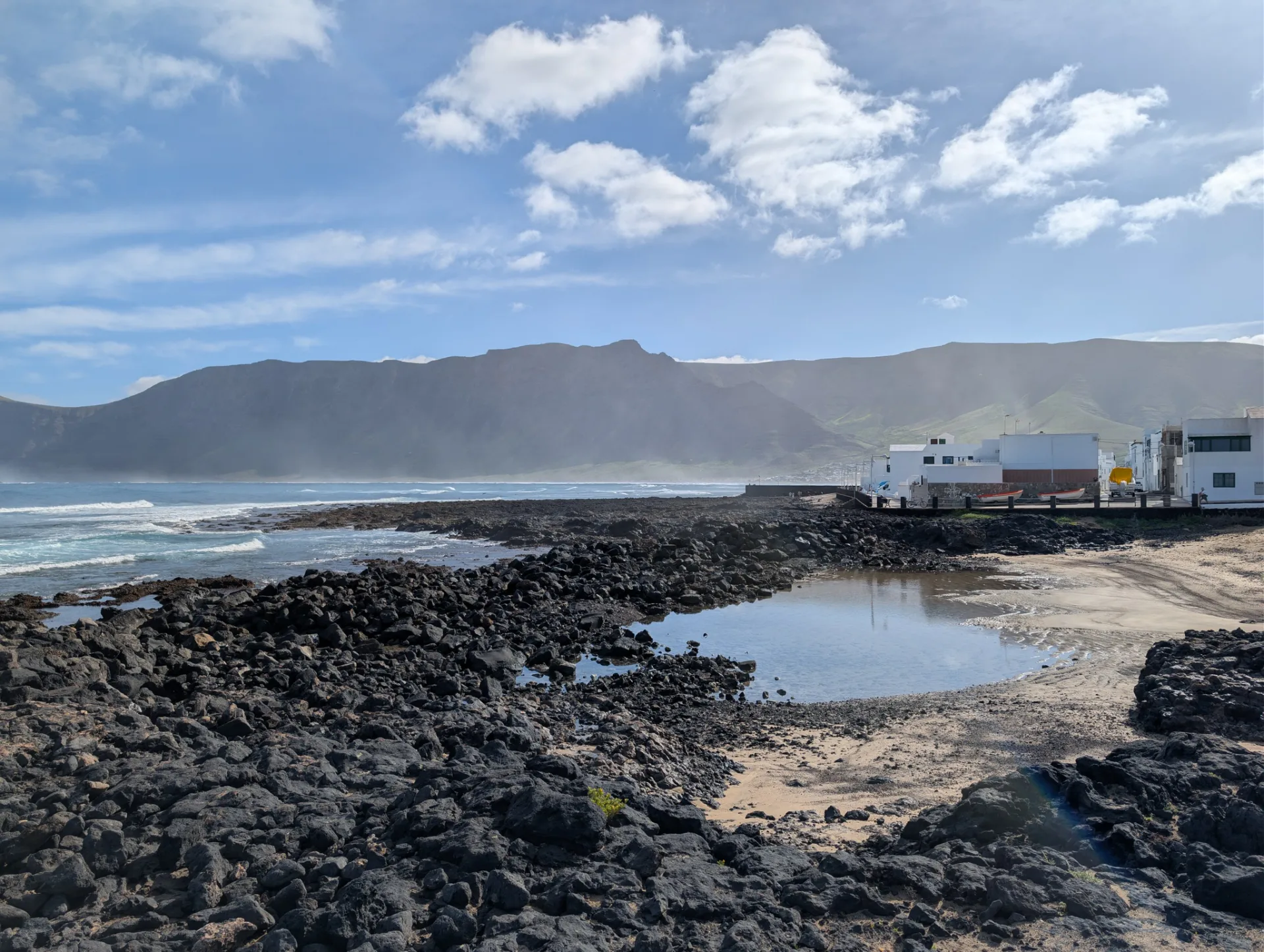 Ein kleiner Küstenort an der Felsküste, dahinter das Famara-Massiv.