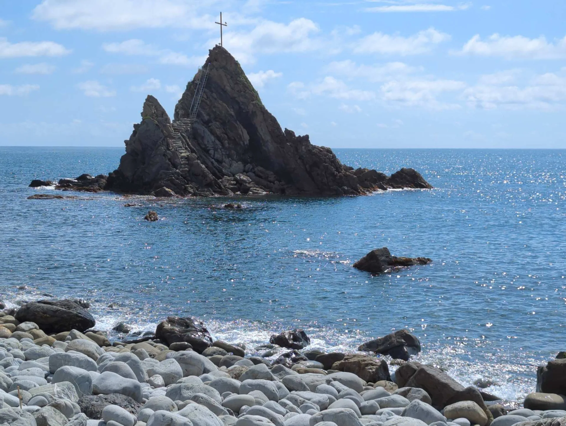 Ein Felsen mit Gipfelkreuz vor der Küste bei Sestri Levante