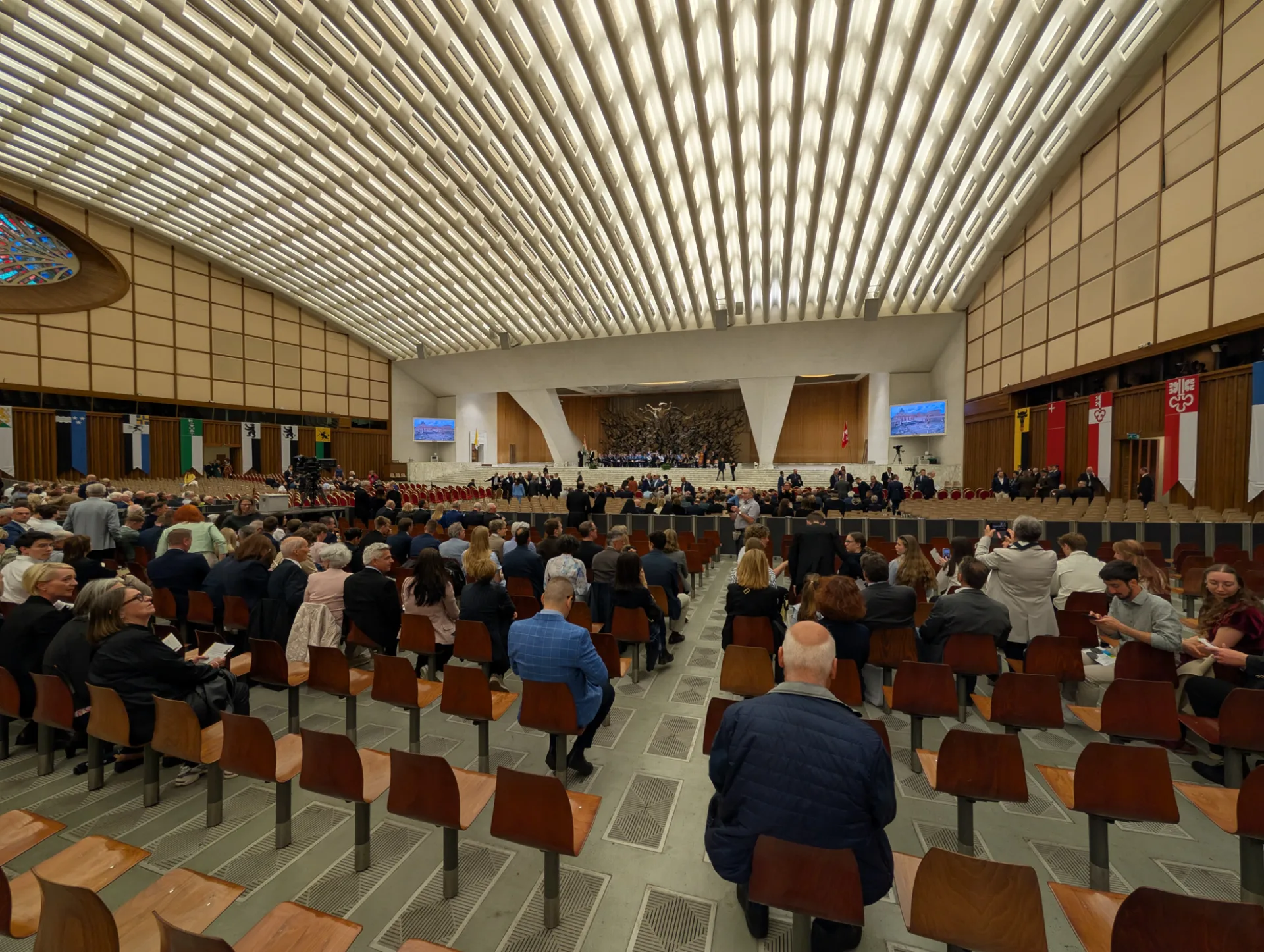 Aula Paolo VI — Stuhlreihen und die rot-gelben Helme der Schweizergarde im Hintergrund
