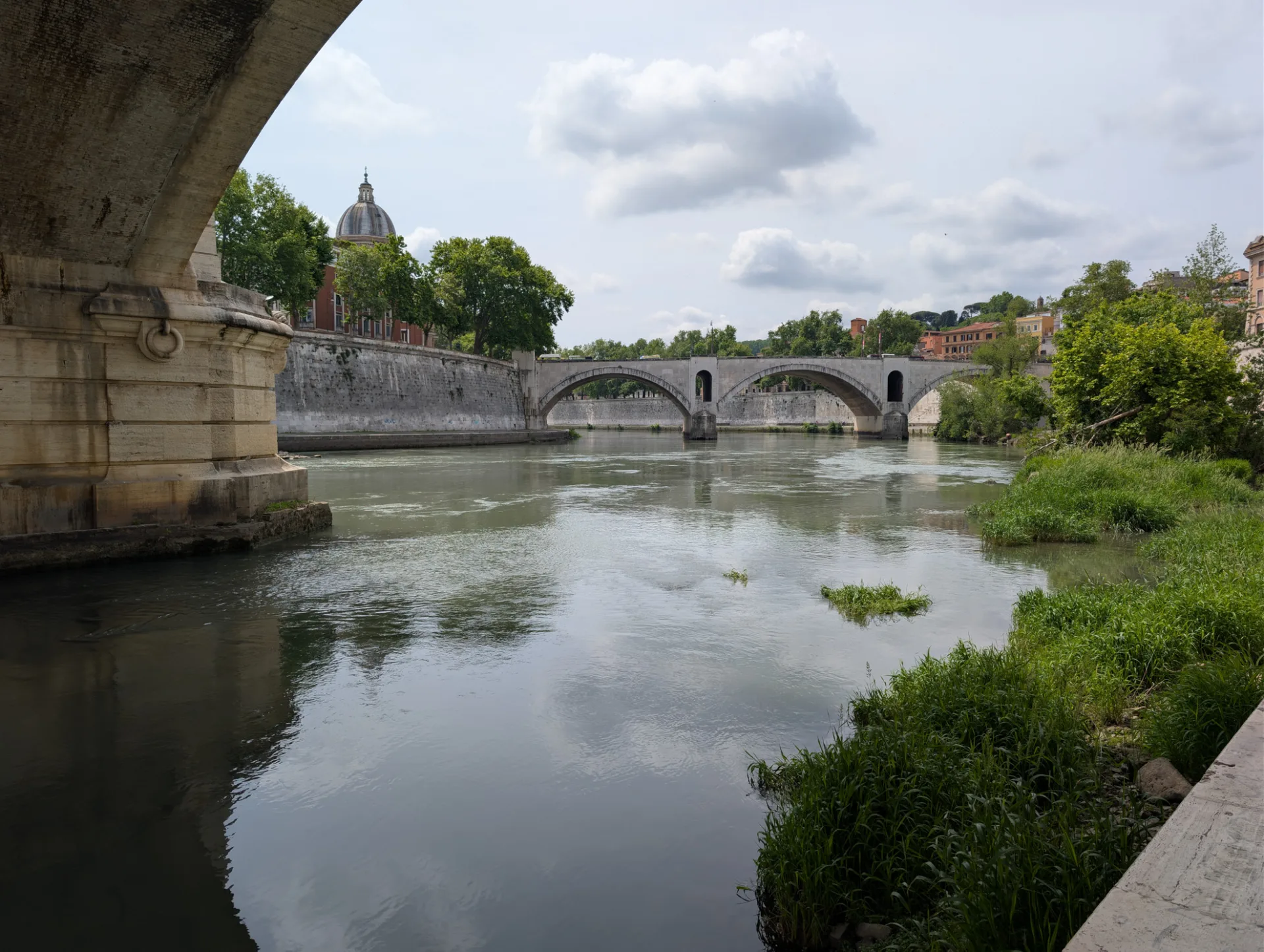 Tiber unter einer Brücke — die Kuppel von San Giovanni Battista im Hintergrund