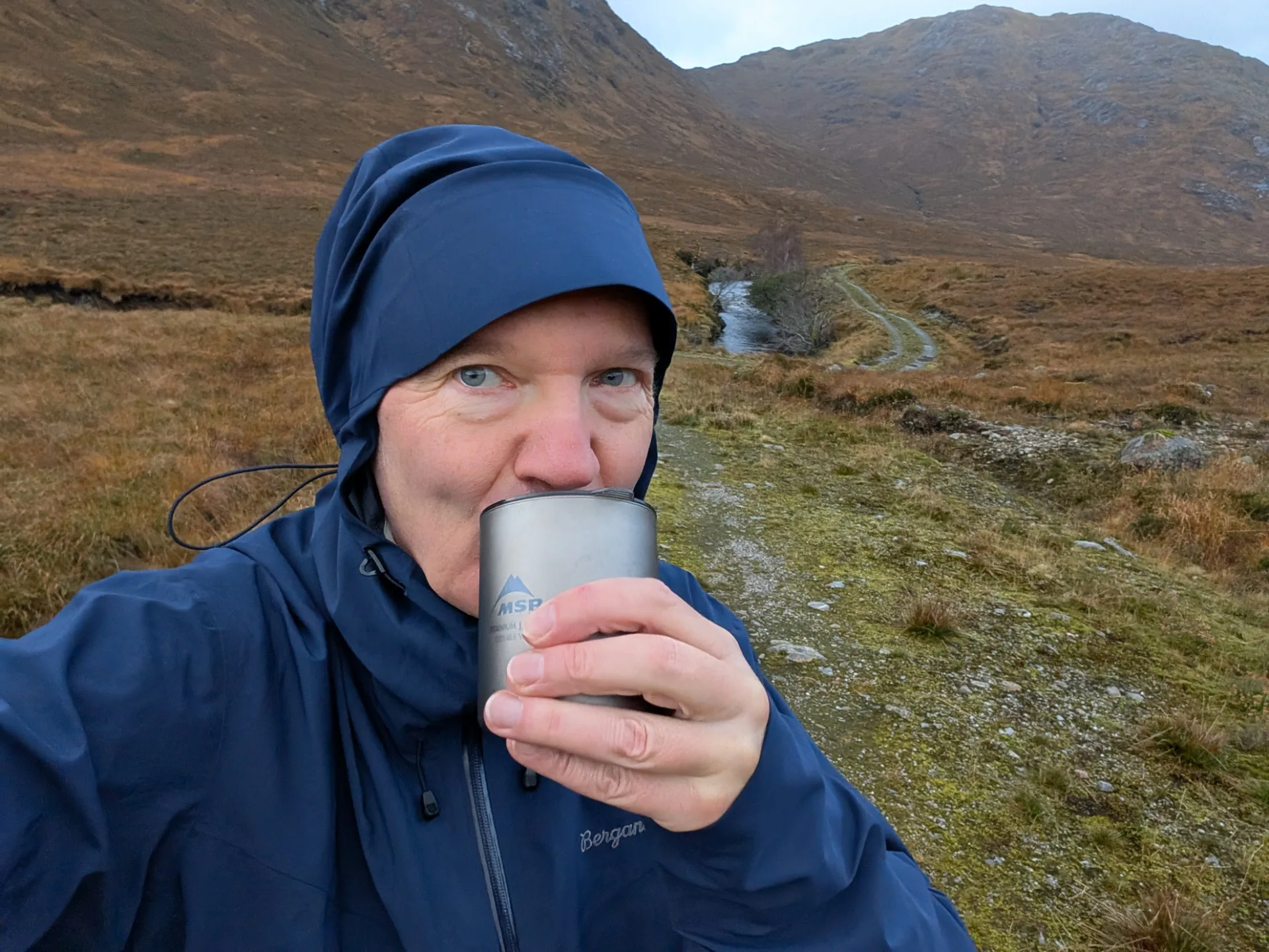 Erste Tasse bei Regen — der Becher dampft, der Pfad zieht sich